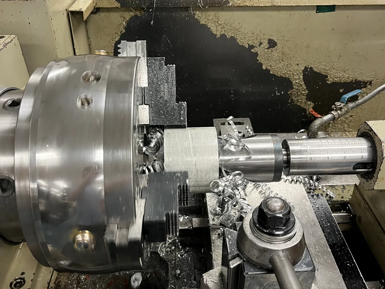 A cylindrical workpiece held in a lathe chuck while a tool cuts into its end, swarf curling away from the cut.