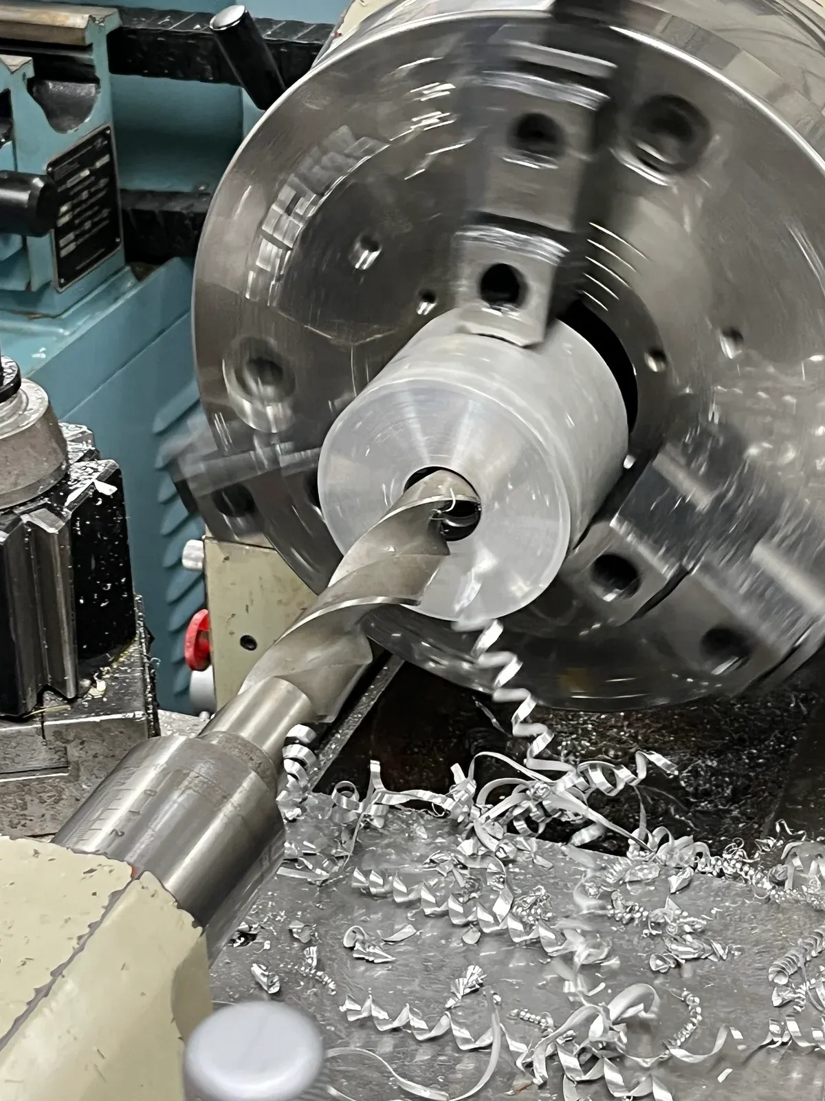 A drill cutting into a cylindrical workpiece held in a lathe.