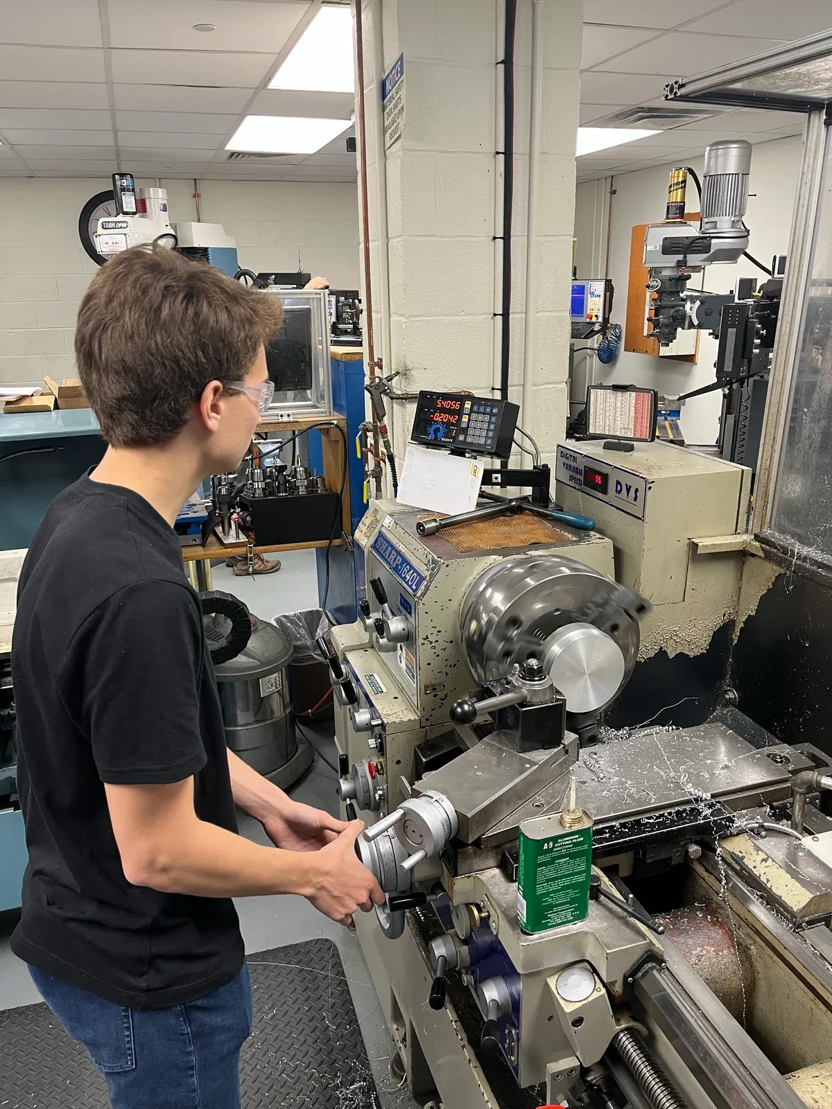 A student operating a lathe while machining a metal part in the shop.